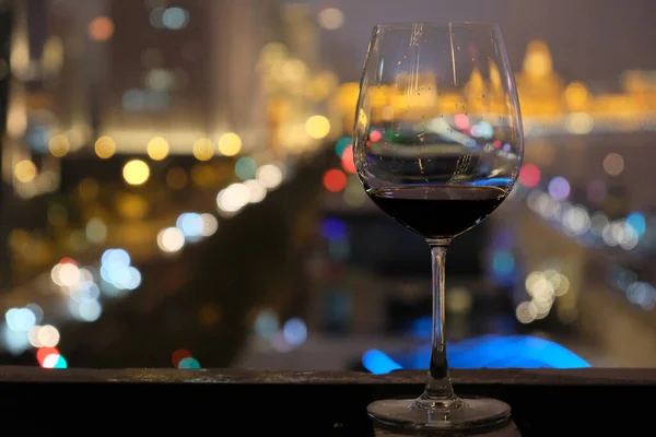close up one glass with red wine inside. Blurred colorful urban night lights background. At The Bund of Shanghai China