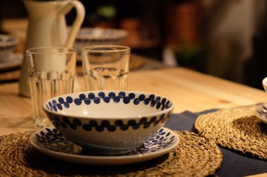 Geceleri porselen kaseyi ve tabağı ahşap yemek masasına kapat. Bulanık içki bardakları ve çaydanlık arka planı