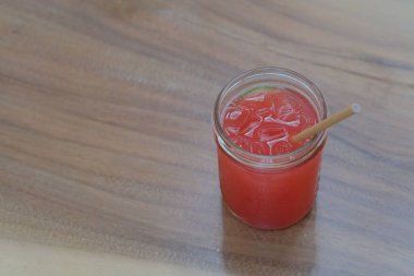 Bir bardak kırmızı meyve suyunu ahşap masada buz küpleriyle kapat. Bulanık arkaplan