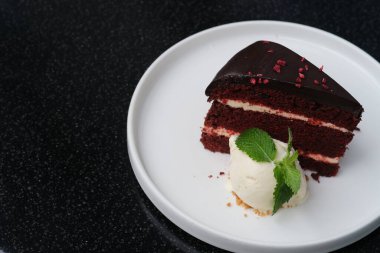 Bir dilim çikolatalı pasta ve dondurmayı siyah masada beyaz tabakta kapat.