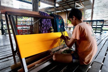 Shan State / Myanmar-Eylül 2019: yerde oturan genç bir adam. Eşarp ve longyi yapmak için pamuk ve ipekle lotus kökü dokudum. Inle Gölü 'nde geleneksel endüstri. Dünyada eşi benzeri yok.