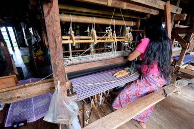 Shan State / Myanmar-Sep.2019: Tahta tezgahta oturan bir kadın Birmanyalı. Eşarp ve longyi yapmak için pamuklu ve ipekli nilüfer kökü kullandım. Inle Gölü 'nde geleneksel endüstri. Dünyada eşi benzeri yok.