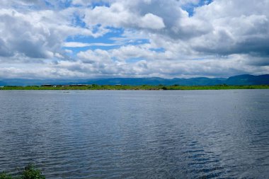 Beyaz bulutlu, güneşli mavi gökyüzünün altında akan Inle Gölü. Geniş açı ve yatay. Shan Eyaleti Myanmar 'da
