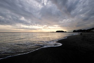 Kanagawa Japonya 'daki Enoshima adasının gün batımı. Deniz dalgaları sahile doğru akıyor. Geniş açı