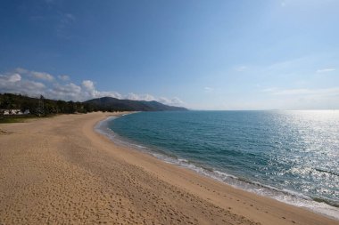  Uzun, boş kumlu sahil şeridi. Hiç kimse. güneşli mavi gökyüzü beyaz bulutlar. yeşil mavi deniz suyu. Beyaz deniz dalgaları. geniş açı
