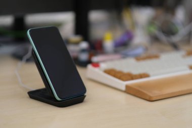 Bir akıllı telefonu dikey kablosuz şarjla kapat. Bulanık klavye ve ofis arkaplanı  