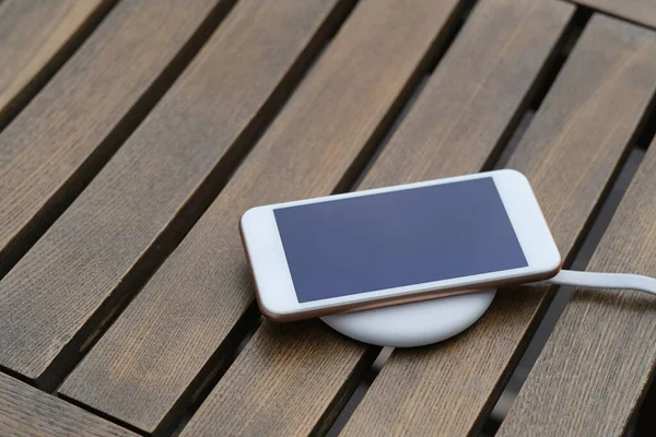 close up one smartphone on wireless charger on wooden table. blur background