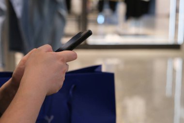 Elbise mağazasında akıllı telefon kullanarak ellerinizi kapatın. Bulanık arkaplan