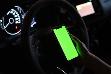 Bir elin yeşil ekranlı akıllı telefonu gece arabada tutarken kapat. Bulanık arkaplan