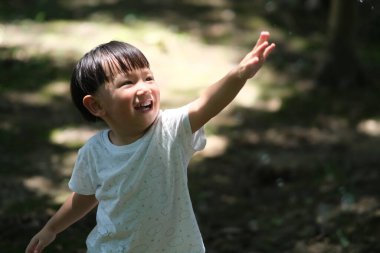 Asyalı bir çocuk güneş ışığına kollarını kaldırıyor. Bulanık arkaplan