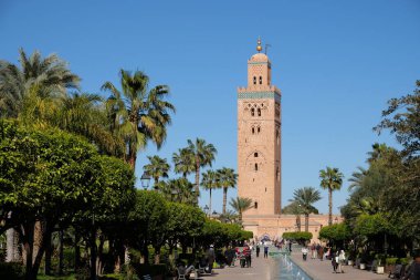 Marakeş / Fas - Nisan 2018: Yeşil ağaçlarla birlikte ünlü kahverengi Koutoubia Camii. Güneşli mavi gökyüzü. Marakeş Fas şehir merkezinde. Marakeş 'teki en büyük cami.