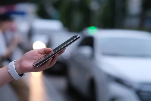 Sokakta akıllı telefon kullanarak elinizi kapatın. Bulanık arabalar arka plan