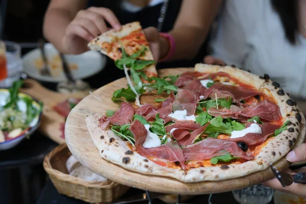 Pizzayı elinle kapamak et, roka ve peynirle birlikte. Tahta tabakta. Odaklanmamış arkaplan