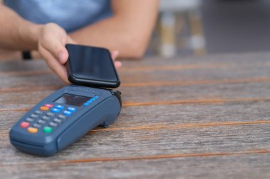 Eski ahşap tezgahtaki Po terminali üzerinden ödeme yapmak için akıllı telefon kullanan insanları kapatın. Odaklanmamış arkaplan