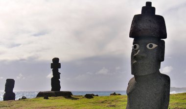 Ahu Tongariki 'nin üç Moai heykeli bulutlu bir gökyüzü, yeşil çimenler ve okyanus, Paskalya Adası (Rapa Nui), Şili