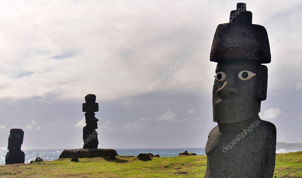 Three Moai statues of Ahu Tongariki against a cloudy sky, green grass and ocean, Easter Island (Rapa Nui), Chile