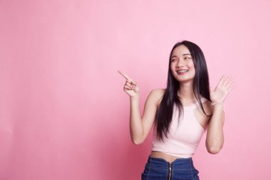 Heyecanlı Asyalı kadın pembe arka plandaki boşluğu işaret ediyor