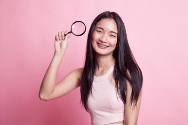 Pembe arka planda büyüteçle genç bir Asyalı kadın.