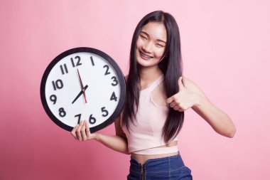 Genç Asyalı kadın pembe arka planda bir saatle onayladı