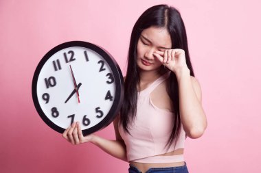 Sabah pembe arka planda saati olan uykulu genç Asyalı kadın.