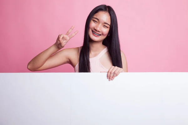 年轻的亚洲妇女在粉红色背景显示胜利标志以空白标志 — 图库照片