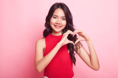 Genç Asyalı kadın pembe arka planda kalp işareti gösteriyor.