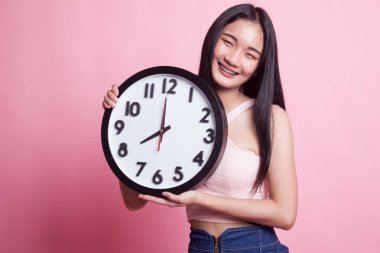 Pembe arka planda saati olan genç bir Asyalı kadın.