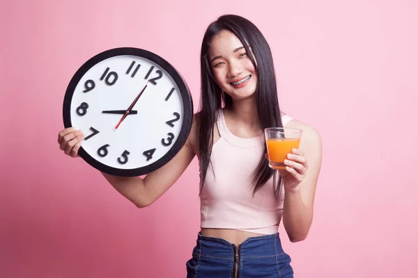 Asian woman with a clock drink orange juice on pink background