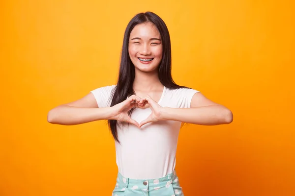 若いアジア女性は 明るい黄色の背景に心手の記号を表示します — ストック写真