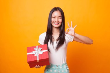 Genç Asyalı kadın parlak sarı zemin üzerine bir hediye kutusu ile Tamam göster