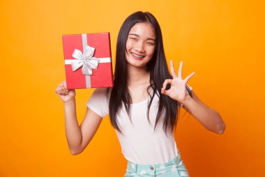 Genç Asyalı kadın parlak sarı zemin üzerine bir hediye kutusu ile Tamam göster