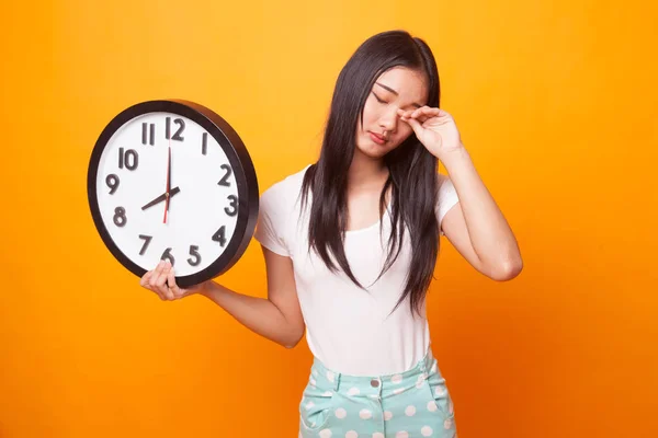 Sleepy young Asian woman with a clock in the morning on bright yellow background
