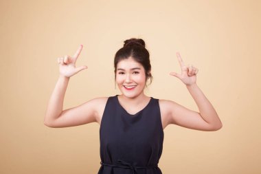 Genç Asyalı kadın bej arka planda boş bir alanı işaret ediyor