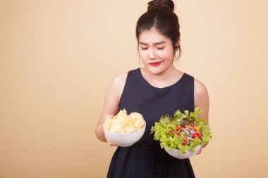Bej arka planda patates cipsi ve salatalı genç Asyalı kadın.