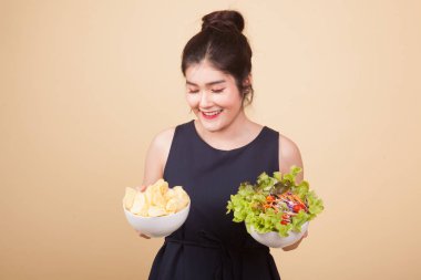 Bej arka planda patates cipsi ve salatalı genç Asyalı kadın.