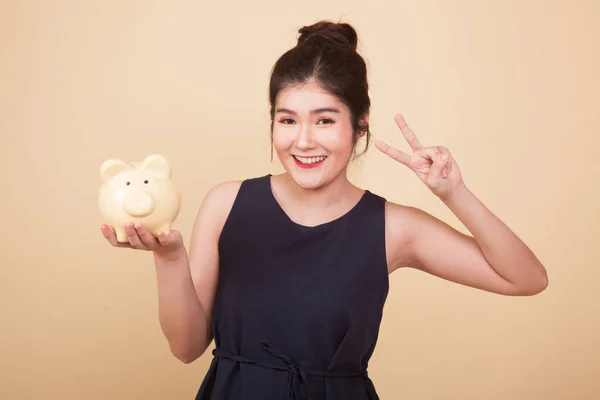 Asyalı Kadın Bej Arka Planda Domuz Sikkesi Bankasıyla Zafer Işareti — Stok fotoğraf