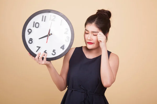 Sleepy young Asian woman with a clock in the morning  on beige background