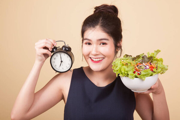 Young Asian woman with clock and salad  on beige background