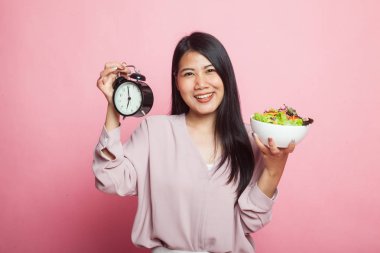 Pembe arka planda saati ve salatası olan genç Asyalı kadın.