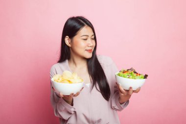 Pembe arka planda patates cipsi ve salatalı genç Asyalı kadın.