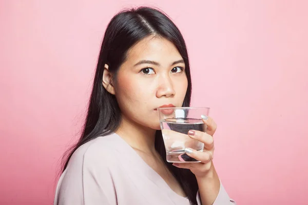 Young Asian woman with a glass of drinking water on pink background