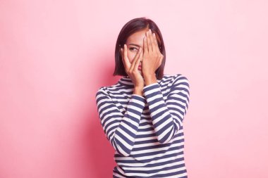 Güzel genç Asyalı kadın pembe arka planda parmaklarının arasından dikizliyor.