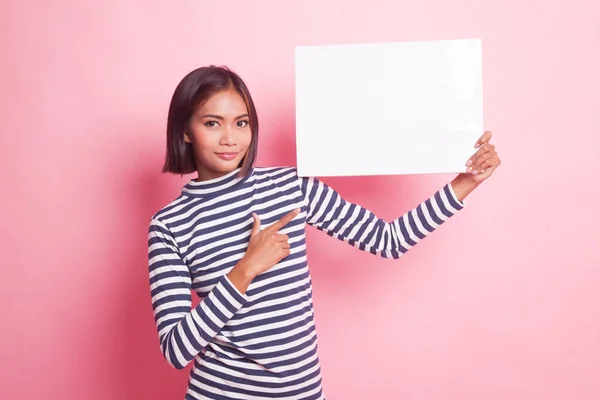年轻的亚洲女人指着粉色背景上空白的标志 — 图库照片