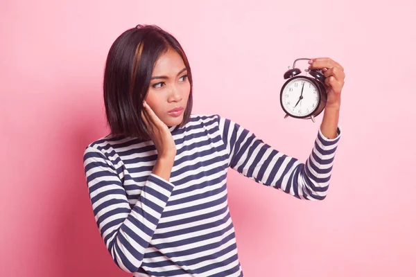 Young Asian woman is stressed with a clock on pink background