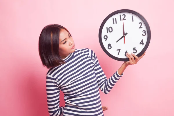 Young Asian woman with a clock on pink background