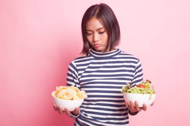 Pembe arka planda patates cipsi ve salatalı genç Asyalı kadın.