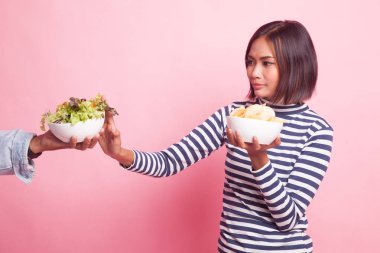 Patates cipsli genç Asyalı kadın pembe arka planda salataya hayır diyor.