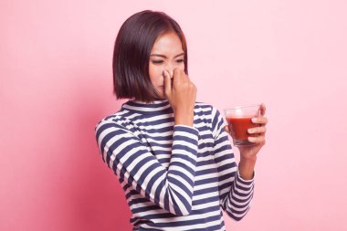 Genç Asyalı kadın pembe arka planda domates suyundan nefret eder.