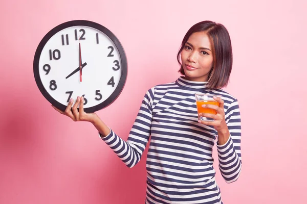 Pembe bir arka plan üzerinde bir saat içki portakal suyuyla Asyalı kadın