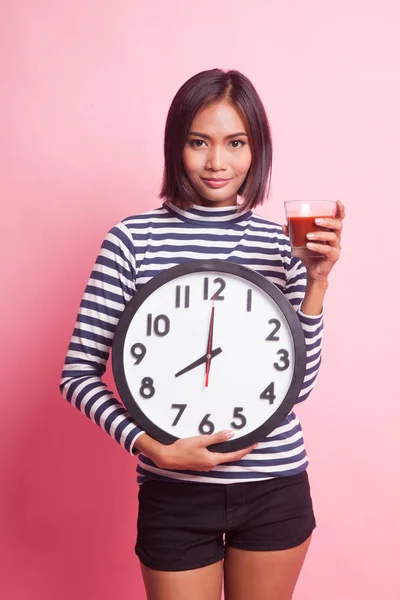 Young Asian woman with tomato juice and clock on pink background